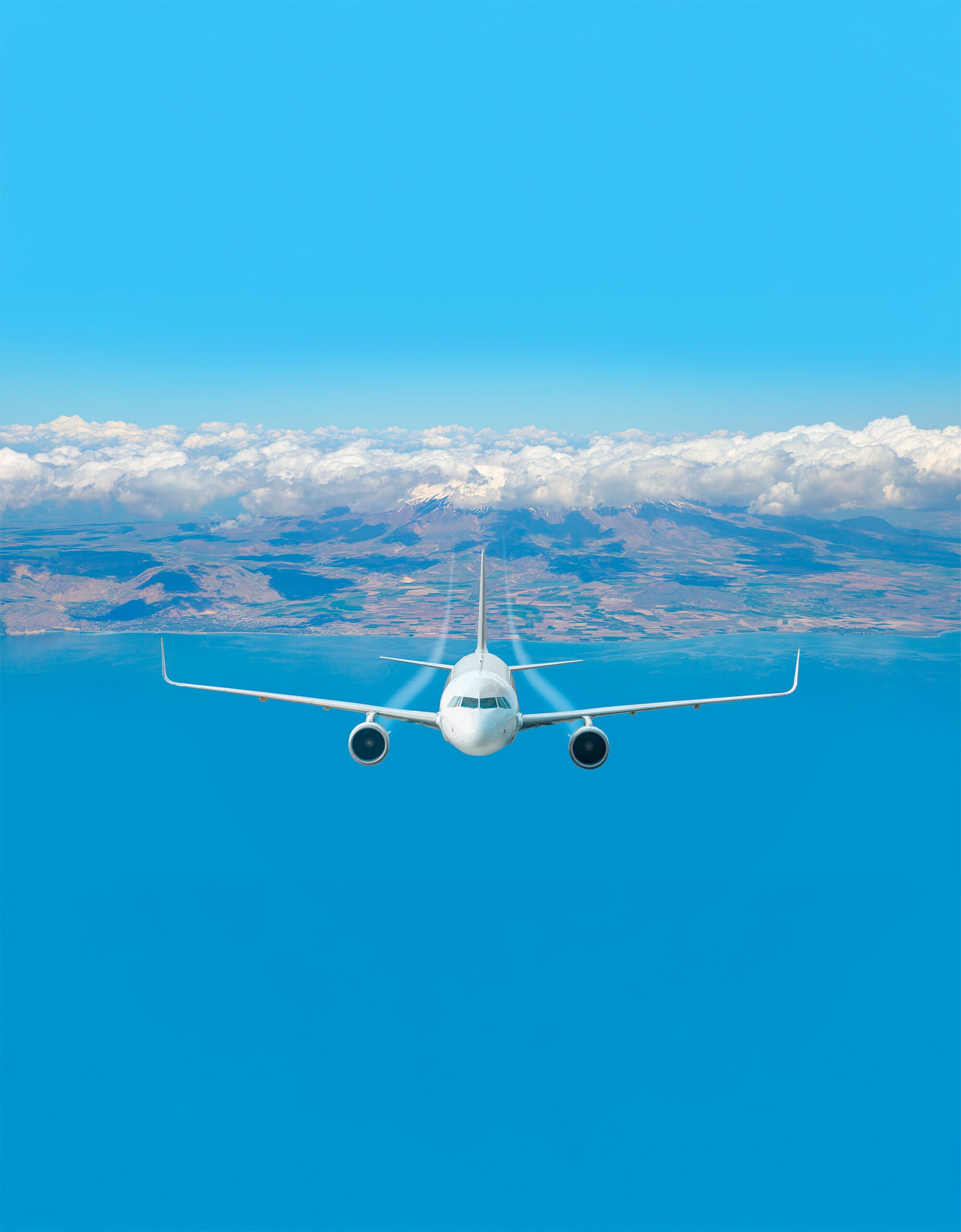 A commercial airplane flies toward the camera above a clear blue sky with distant mountains and clouds visible below, highlighting air travel.